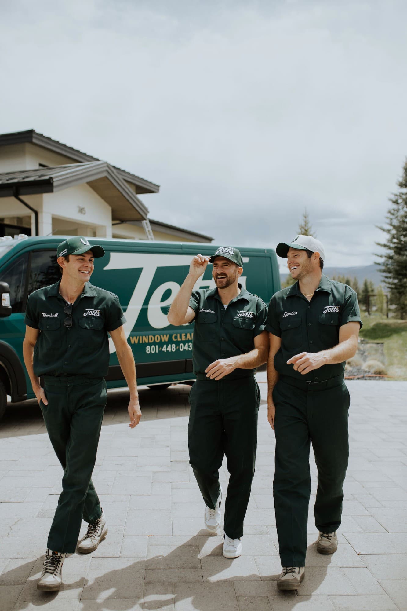 Three Jett's crew members in green uniforms walking in front of a Jett's Window Cleaning van